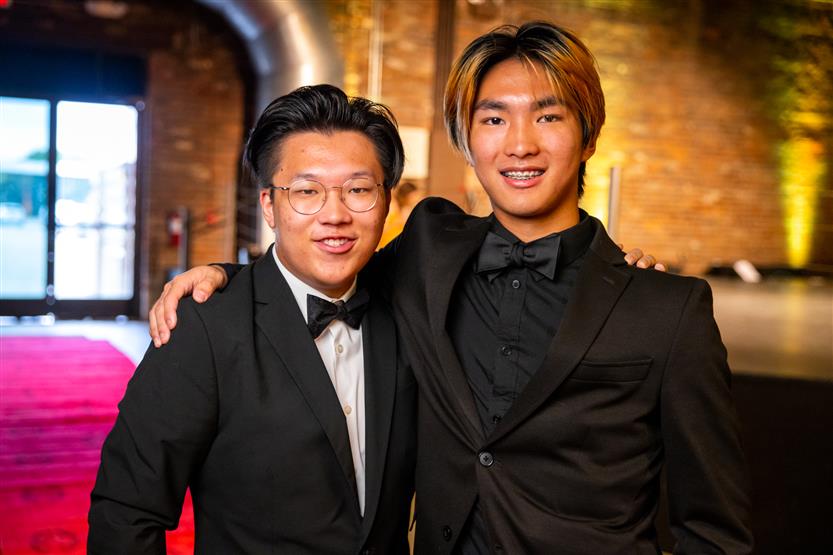 Two young men wearing tuxedos smile